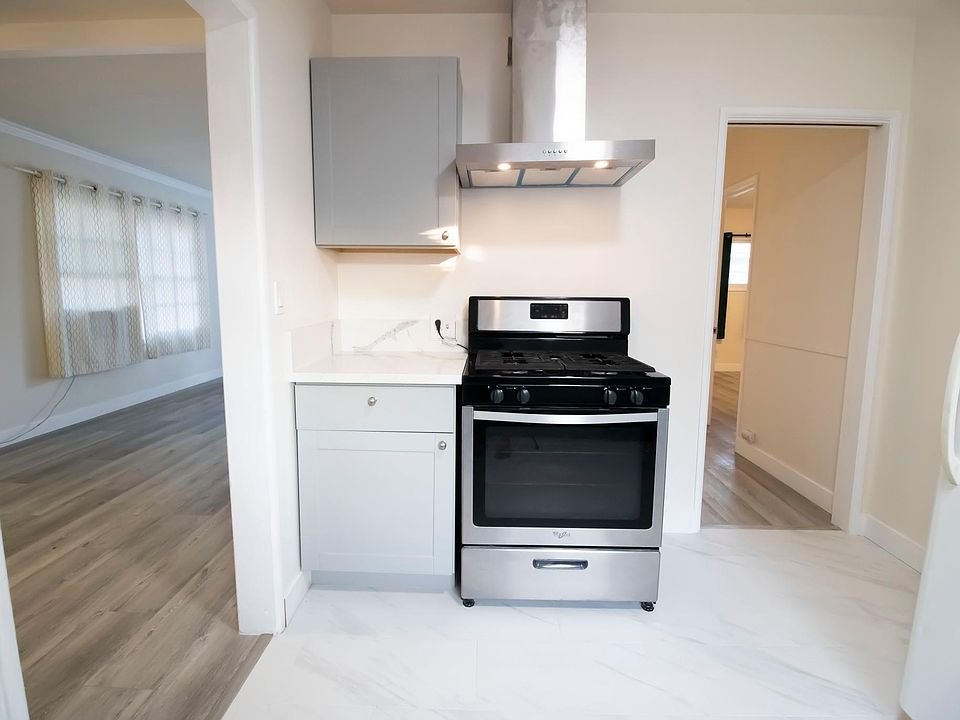 Modern kitchen in California with a stainless steel gas stove and range hood, light gray cabinets.