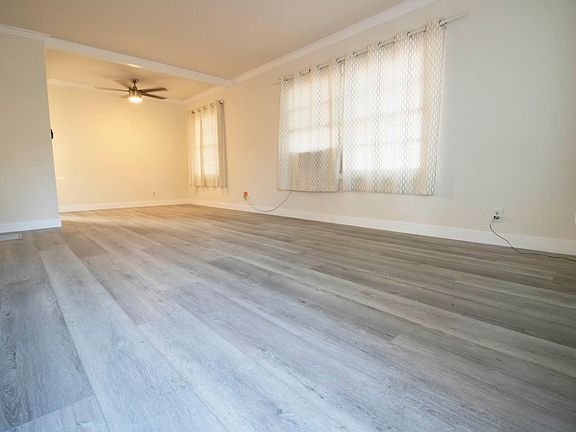Empty room features light gray wood flooring, cream walls, and large windows in California