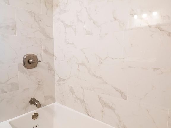 Marble-tiled bathroom wall with silver shower fixtures and a bathtub in California