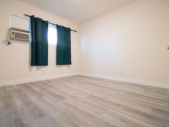 Empty room with light wood flooring, beige walls, and a small window with dark curtains in California.