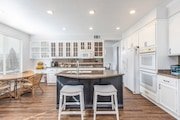 Modern kitchen in California with white cabinets, a central island with two stools.