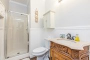 Bathroom with white walls glass-enclosed shower, toilet, and ornate wooden vanity in California.