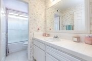 Bathroom in California with floral wallpaper, large mirror, white counter, and glass shower door.