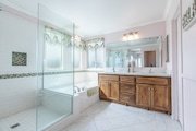 Bathroom in California with glass shower, large bathtub, and wooden vanity.