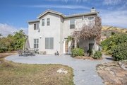 Two-story house in California with light gray exterior set with patio and chairs.