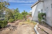 Backyard with sparse grass and a stone path next to a house in California.