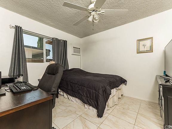 Bedroom in California house with tiled floor, bed, desk with computer, air conditioner, ceiling fan, and wall art