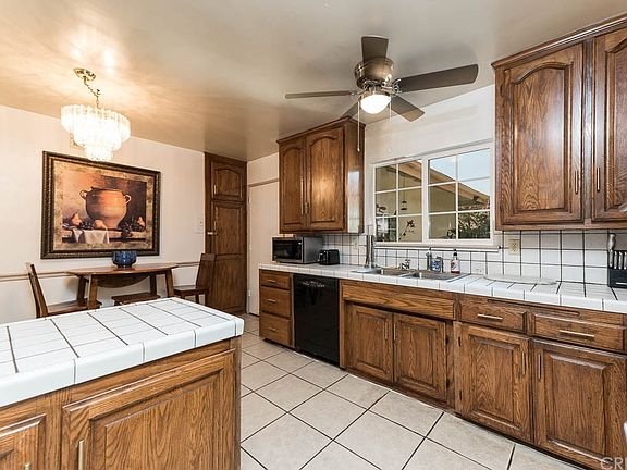 Kitchen with wooden cabinets, white tile countertops, and tiled floor in California