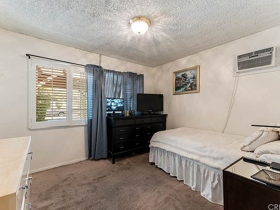 Bedroom in California with beige walls and carpet with a single bed with white bedding.