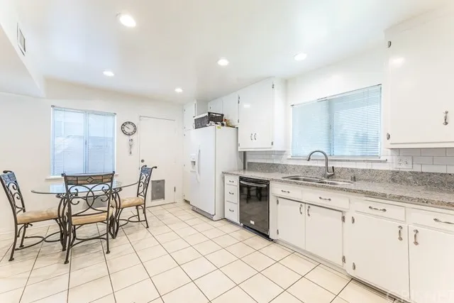 Kitchen in California with white cabinets and tiled floor and glass dining table.