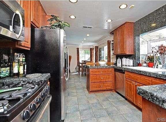 Kitchen in California with stainless steel appliances, dark granite countertops, and wooden cabinets.