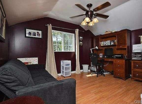 Home office in California with maroon walls, a black sofa, wooden desk with a computer.