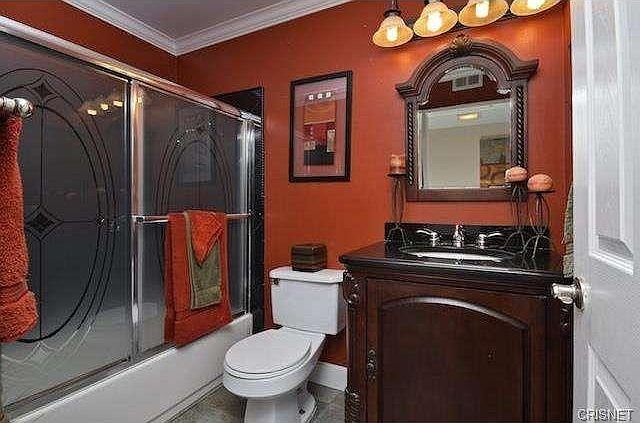 Bathroom with mirror, dark wooden vanity, black countertop, and glass shower doors in California